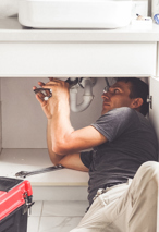 Plumber working under a sink with his tools and red toolbox