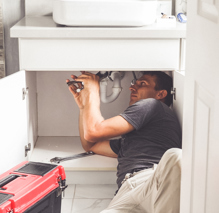 Plumber working under a sink with his tools and red toolbox