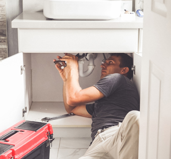Plumber working under a sink with his tools and red toolbox